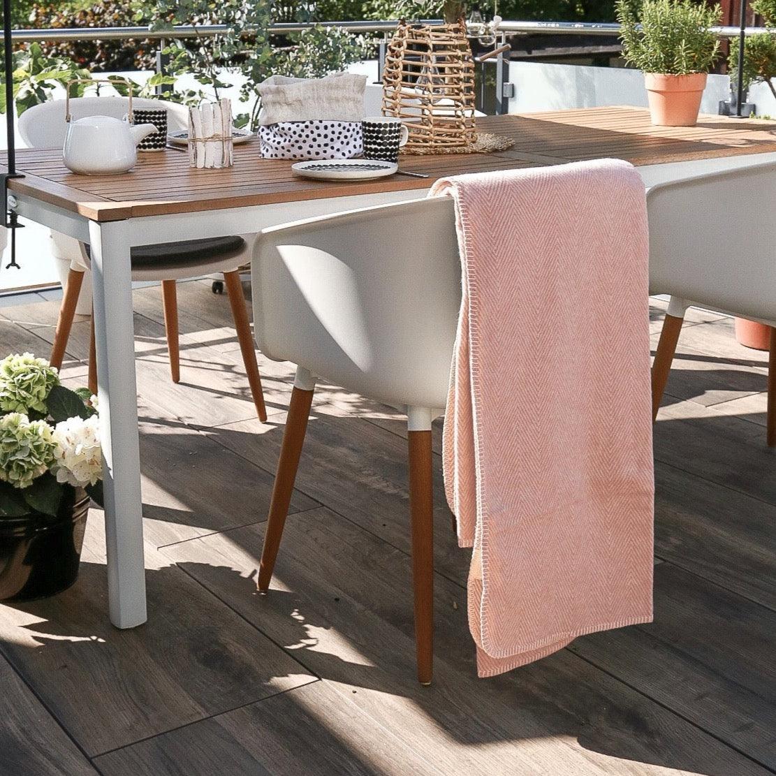Rosafarbene Baumwolldecke über einen weißen Stuhl gelegt auf einer Terrasse