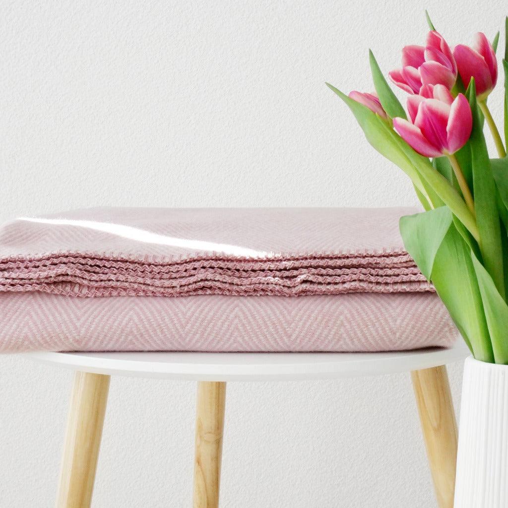 Rosafarbene Wolldecke auf einem weißen Hocker liegend und einem danabenstehendem Blumenstrauß