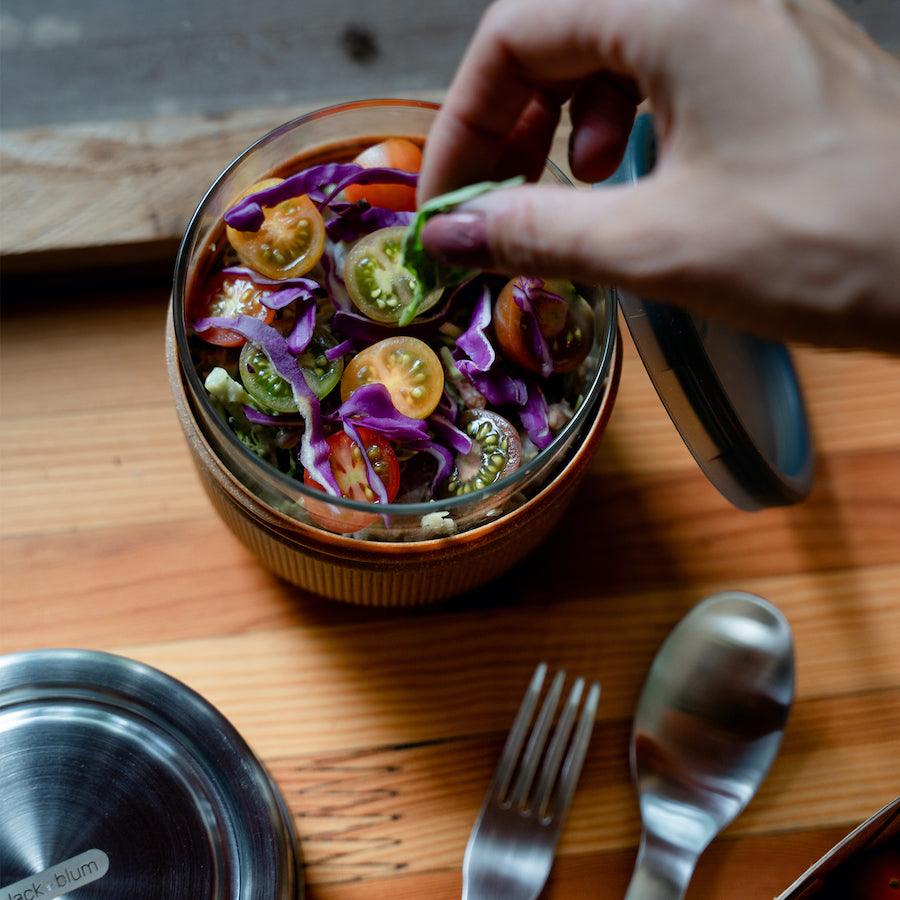 Person gibt Basilikum in Tomatensalat, der in eine runde Glas Bowl gefüllt ist