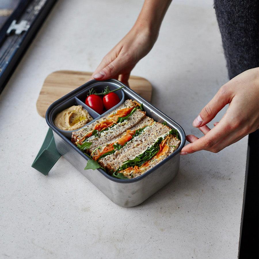 Große Sandwich Box aus Edelstahl mit Sandwiches und Tomaten auf einem Tisch stehend