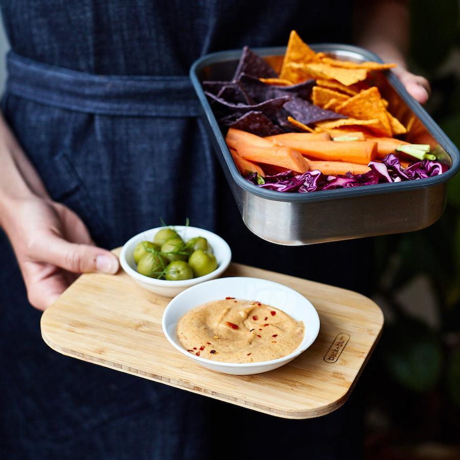 Person mit gefüllter Edelstahl Sandwich Box mit Nachos in der Hand und Bambusdeckel mit Dips