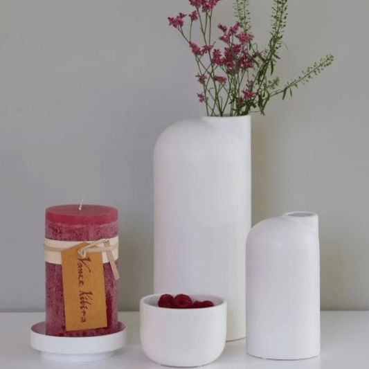 Große weiße Keramikvase mit Blumen neben kleinerer weißer Keramikvase und einer roten Kerze