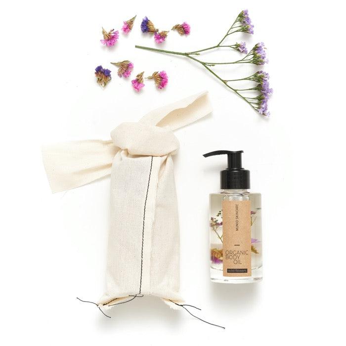 Bio Body Öl in Flasche mit Spender neben Stoffverpackung und Wildblume