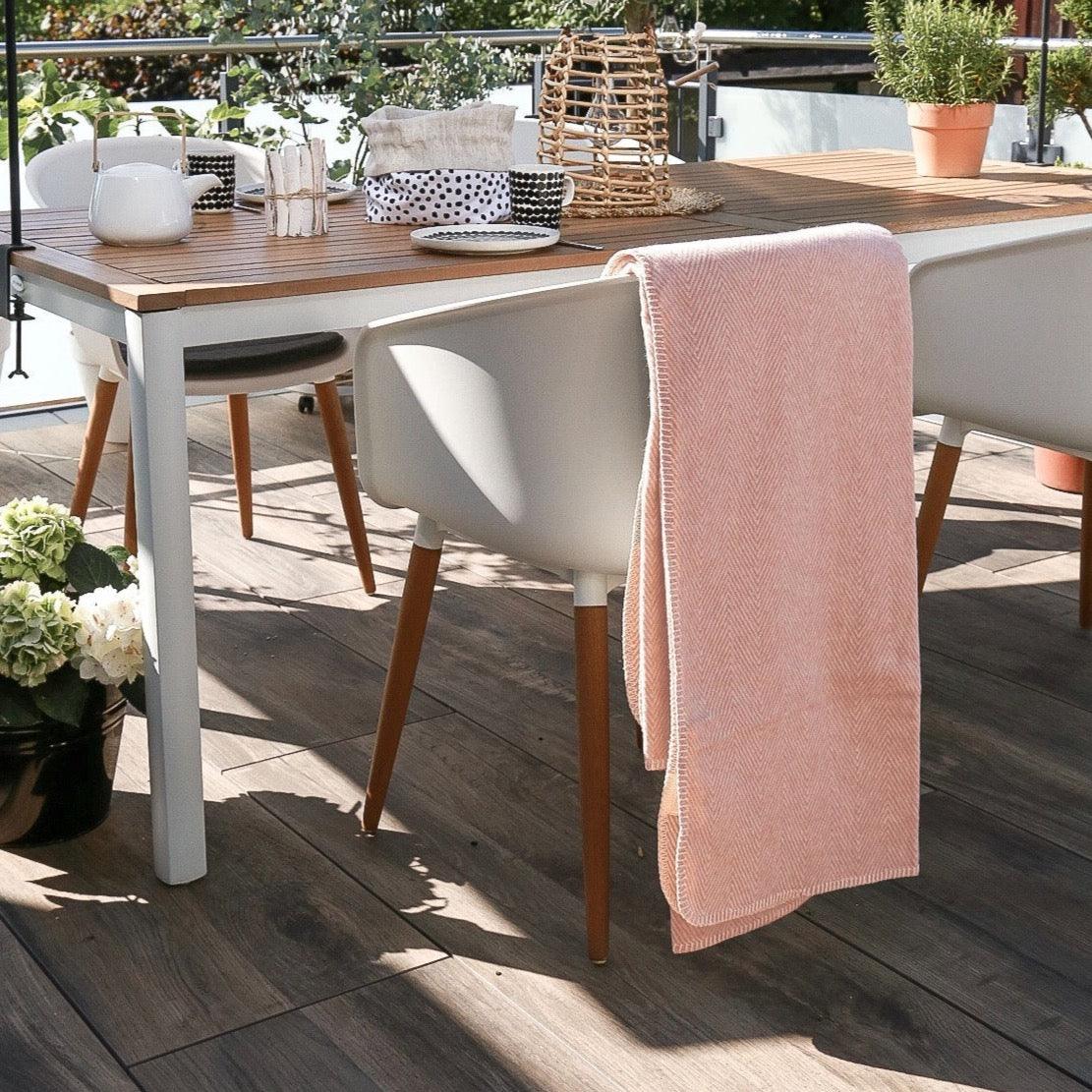 Rosafarbene Baumwolldecke über einen weißen Stuhl gelegt auf einer Terrasse 