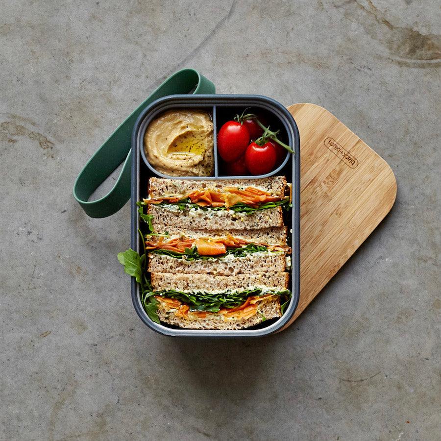 Geöffnete Sandwich Box mit Brot und Tomaten gefüllt auf Bambusdeckel stehend