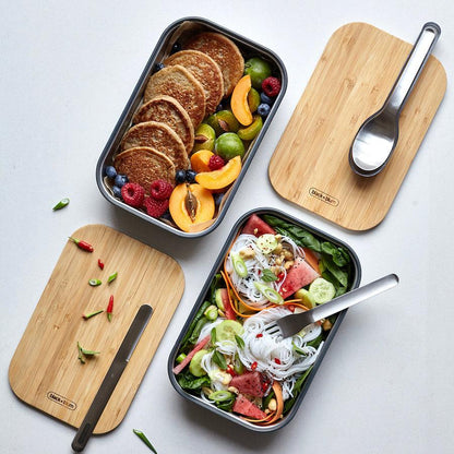 Zwei geöffnete Sandwich Boxen mit Pancakes und Salat befüllt neben Bambusdeckel
