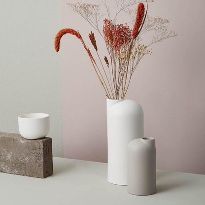 Weiße Keramikvase mit roten Trockenblumen neben kleinerer sandfarbener Keramikvase ohne Blumen