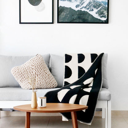 Sofa in einem Wohnzimmer stehend mit schwarz weißer Baumwolldecke darauf liegend und Beistelltisch aus Holz im Vordergrund